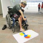Irineu, paciente da Unidade de Longa Permanência, pintando quadro com os pés, para venda no Feirão de Artesanato